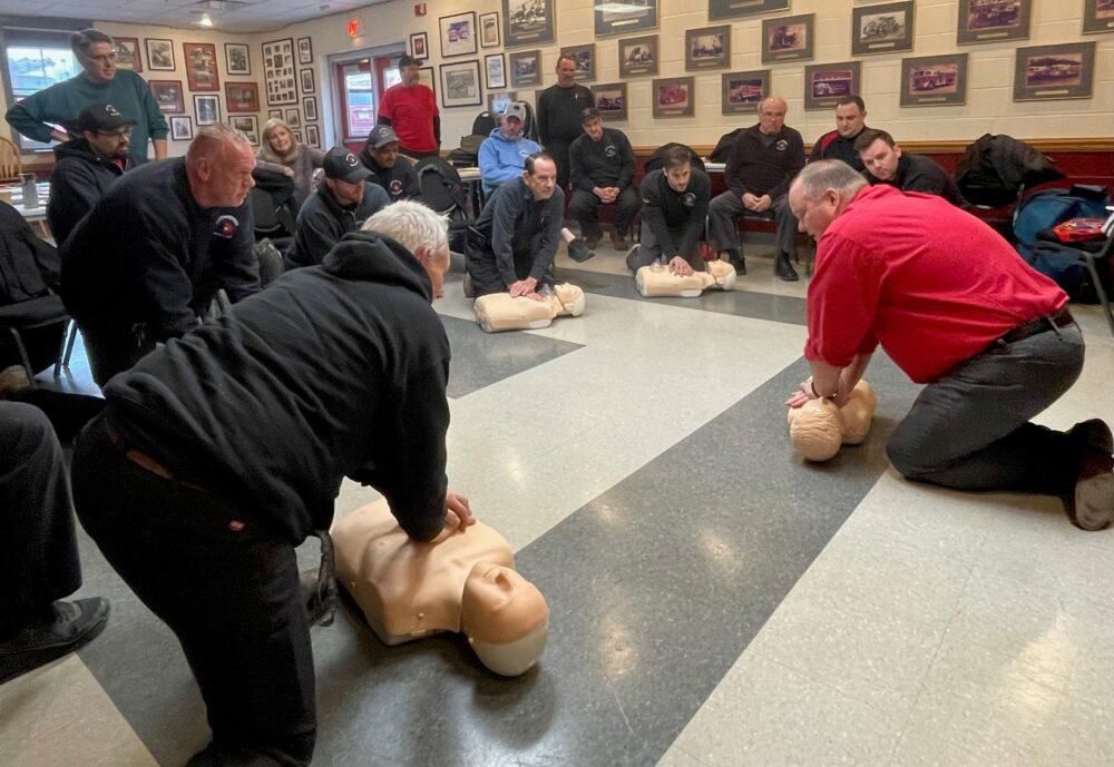 A group of men are practicing on a mannequin in a room.
