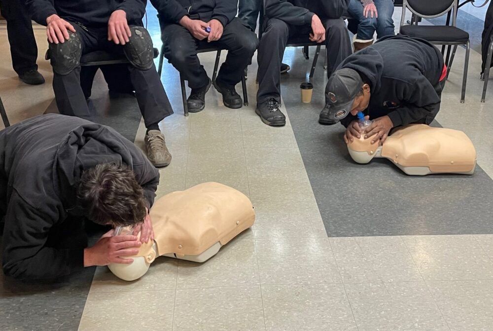 A group of men are kneeling on the floor and practicing a heart massage on a mannequin.