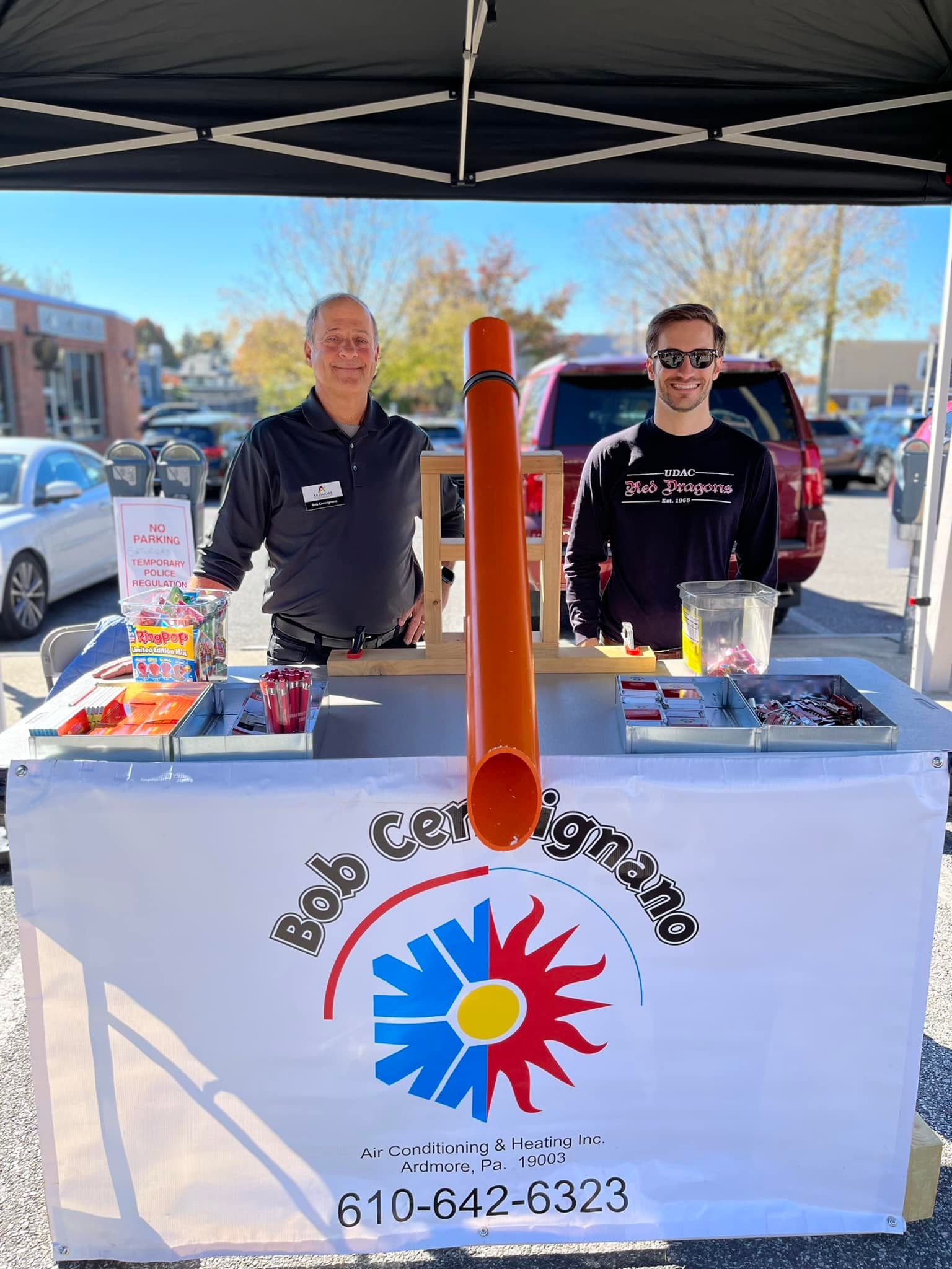 Two men are standing behind a table in a parking lot.