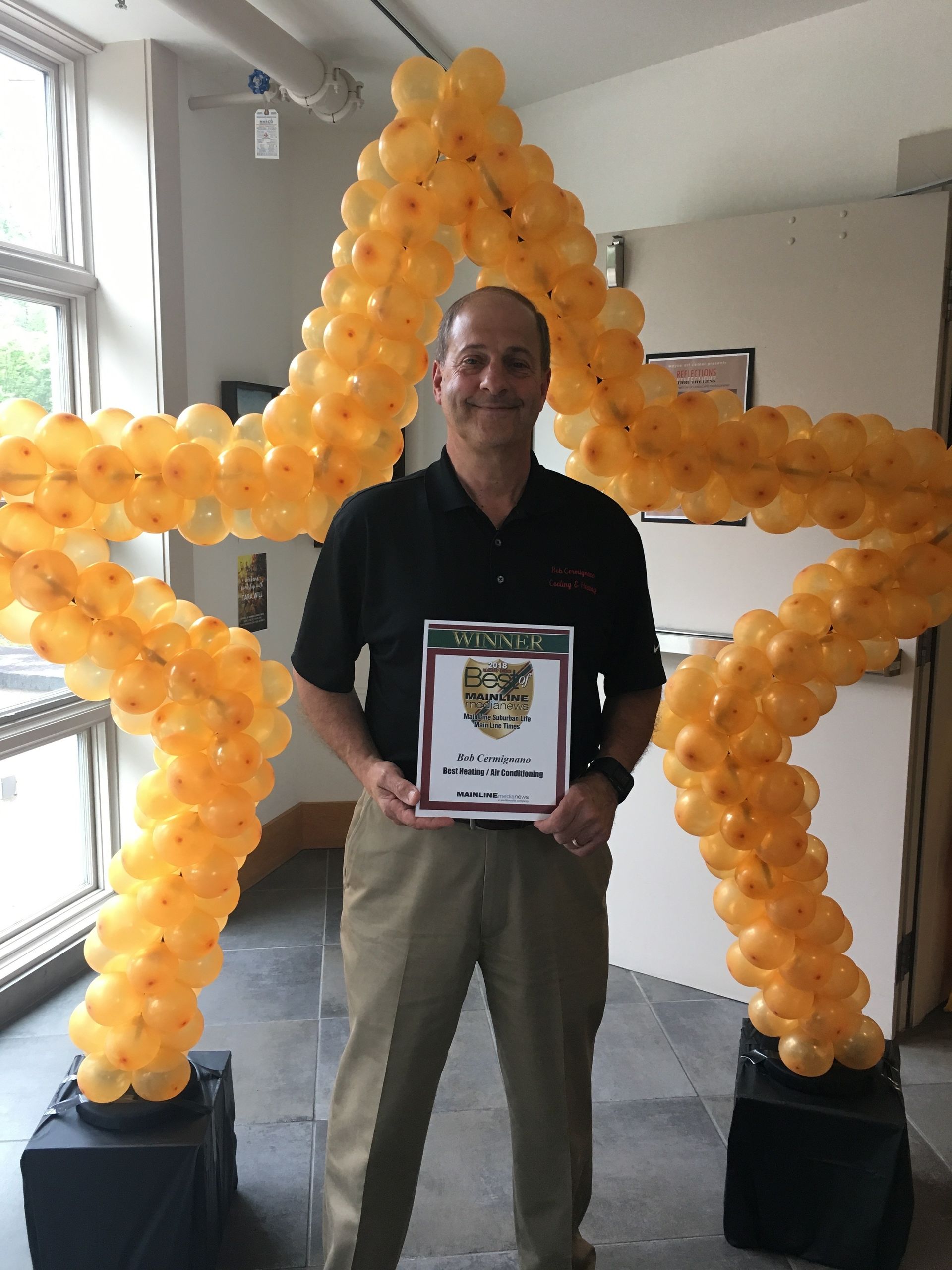 A man is holding a certificate in front of a star made of balloons