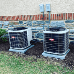 Two bryant air conditioners are sitting in front of a stone wall