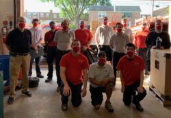 A group of men wearing face masks are posing for a picture in a garage.