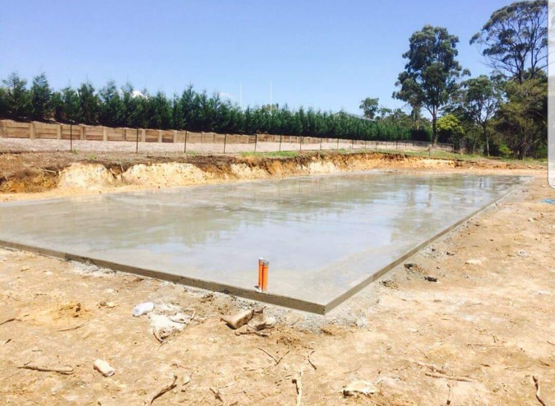 Concrete water reservoir under construction with muddy water and trees in the background