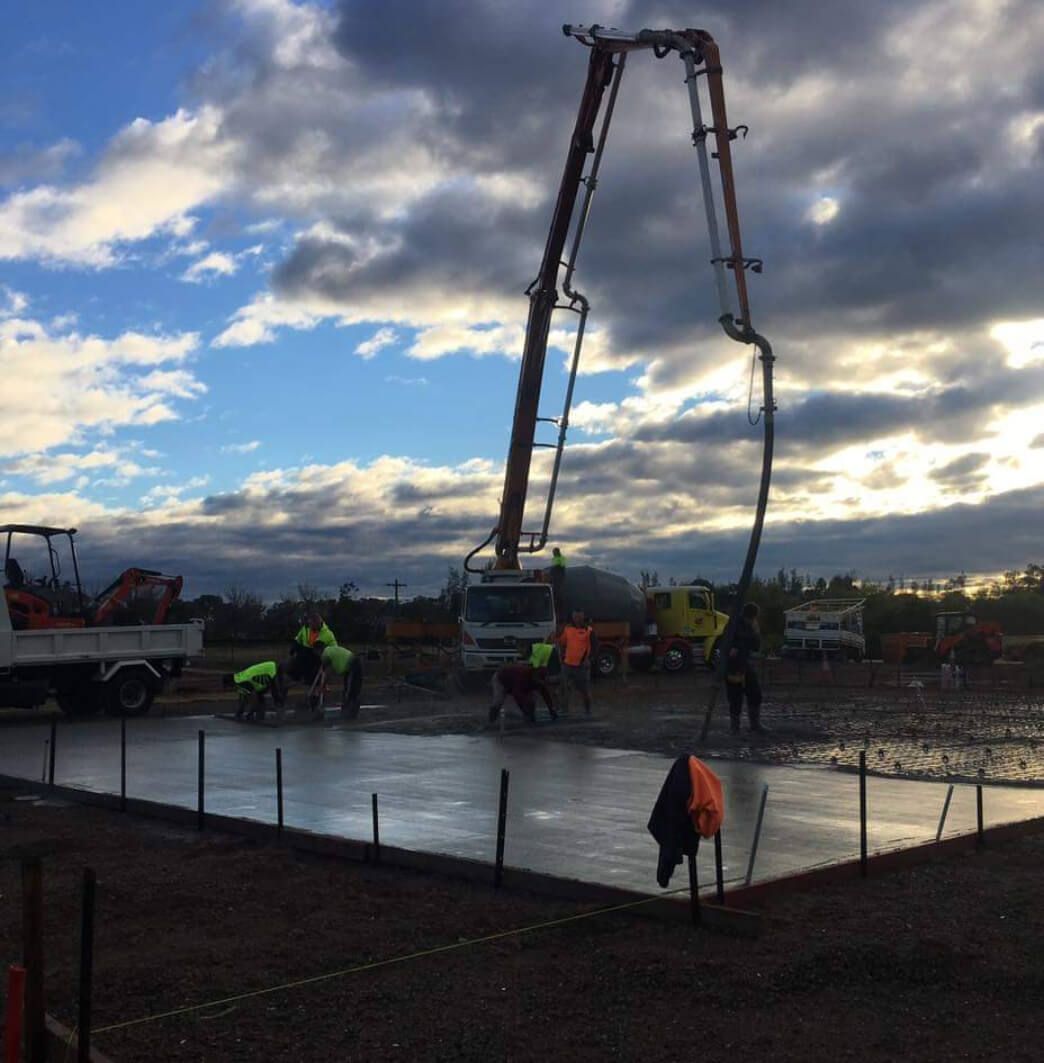 Construction workers pour concrete with a pump boom on a cloudy day.