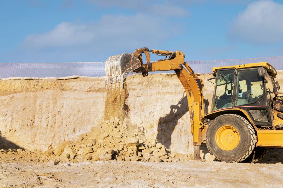 Yellow excavator digging into a sandy cliff at a construction site under a clear sky