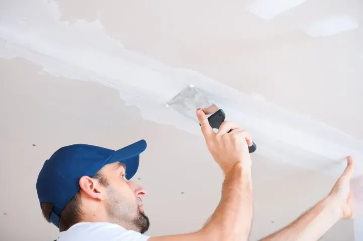 Contractor applying joint compound to a drywall ceiling.