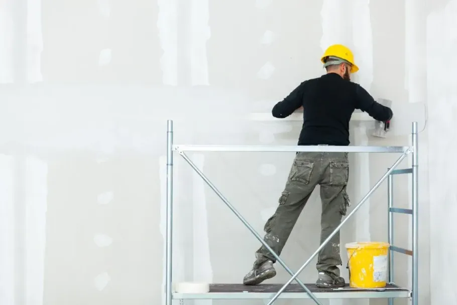 Drywall worker on scaffolding taping a finished wall