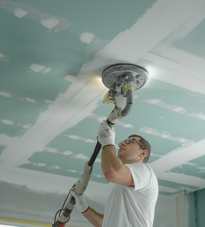 Professional electric drywall sander smoothing a ceiling. 