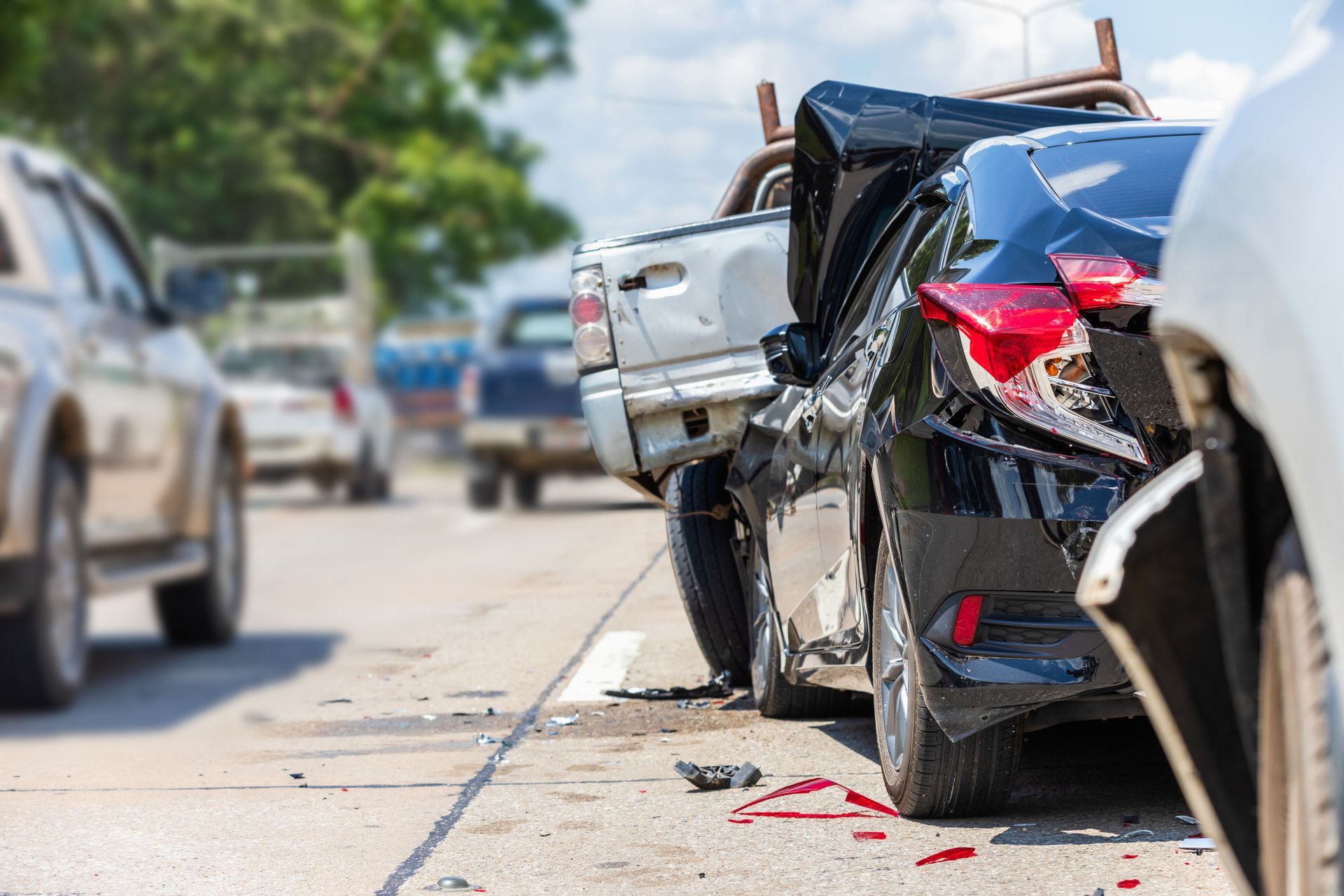 Rear-end car crash on a street, with damaged black sedan and white vehicle, debris on the road.