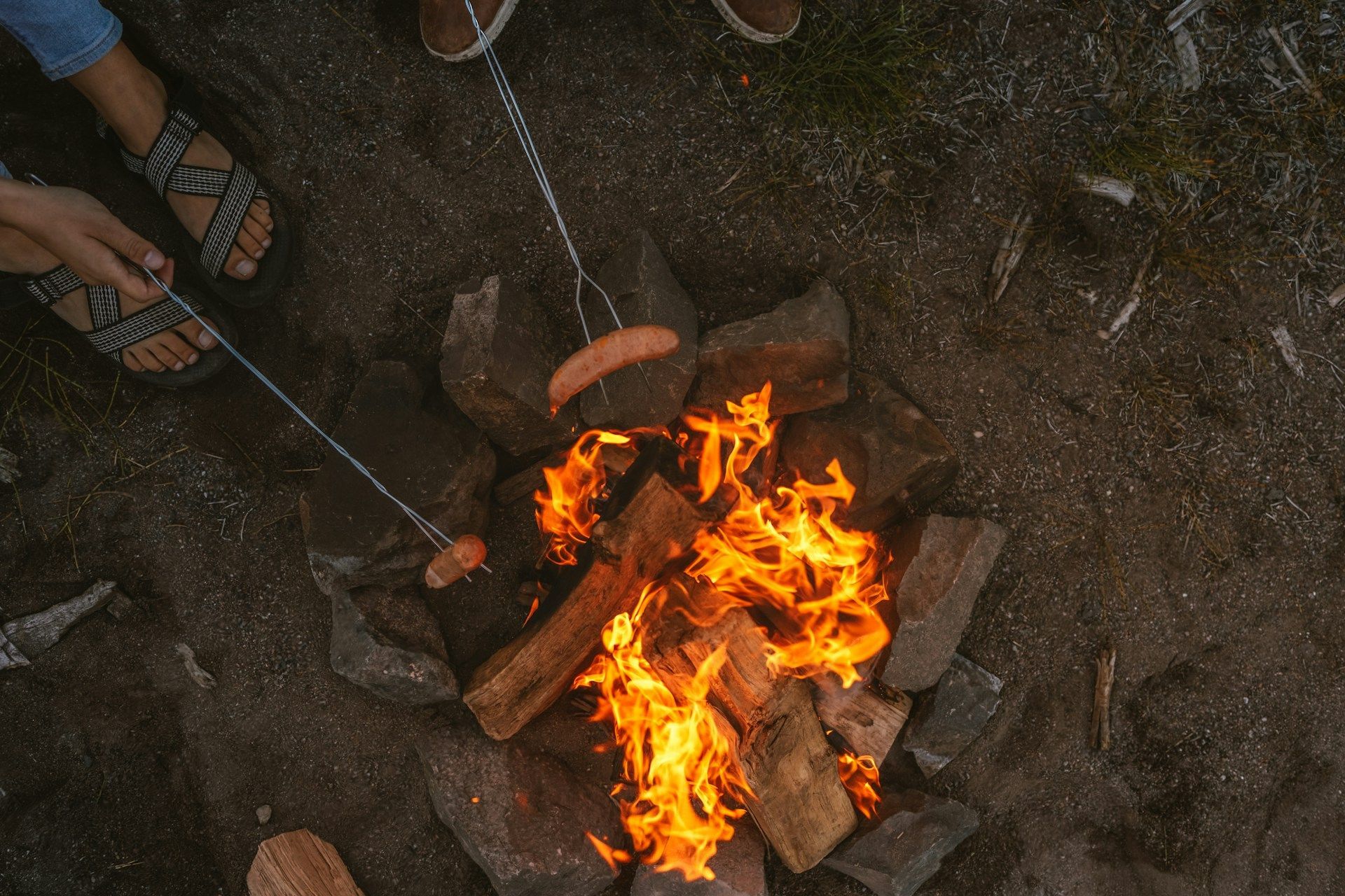 Small campfire burning among rocks, with people’s feet and sandals visible around it.