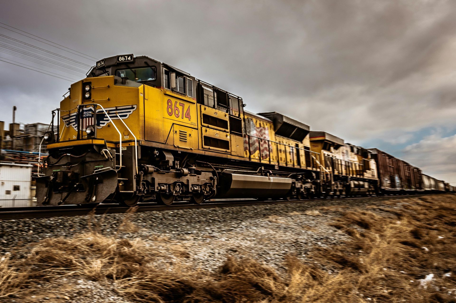 Yellow freight train on tracks under a cloudy sky, stretching into the distance