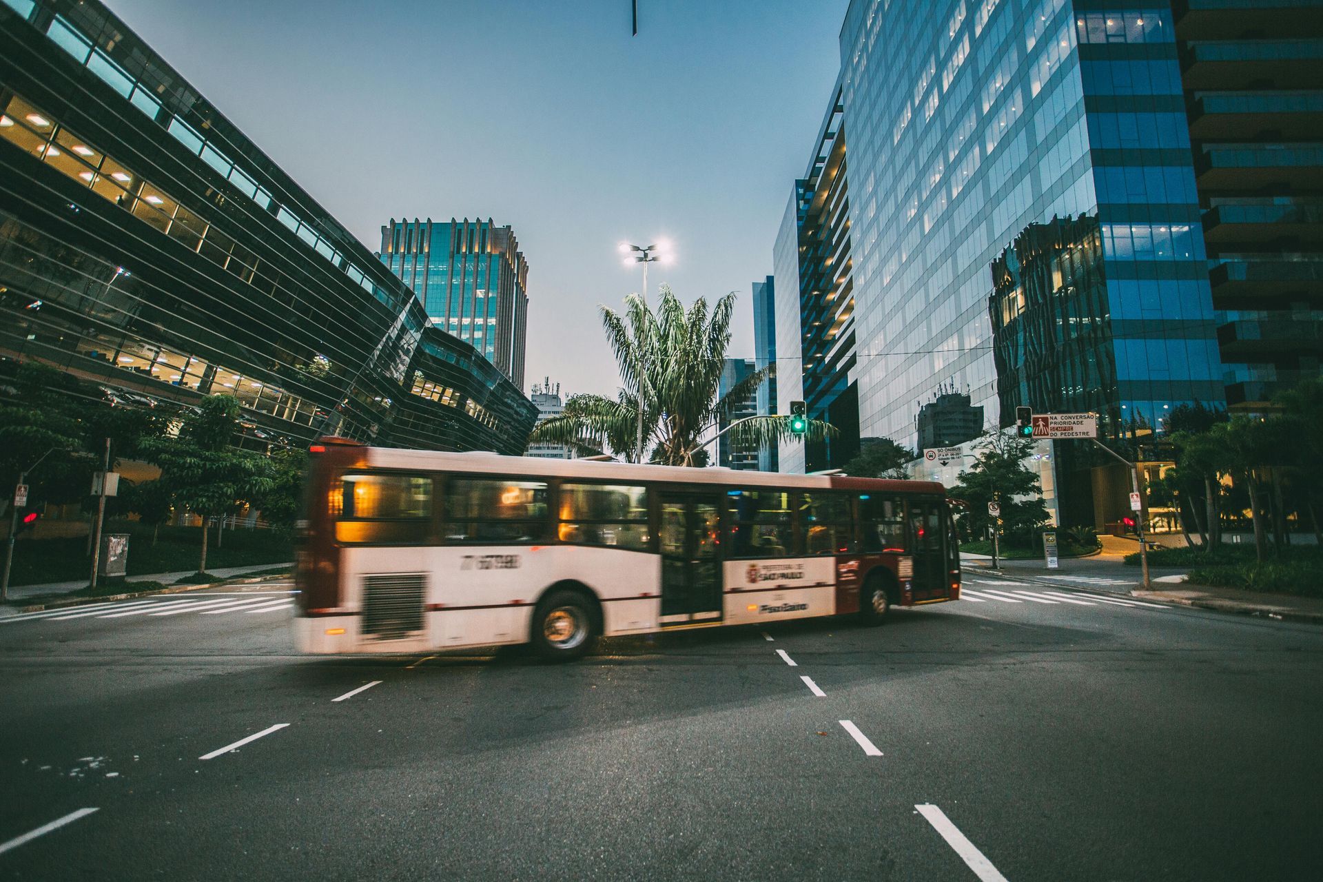 Bus turning through a city street lined with tall glass office buildings at dusk