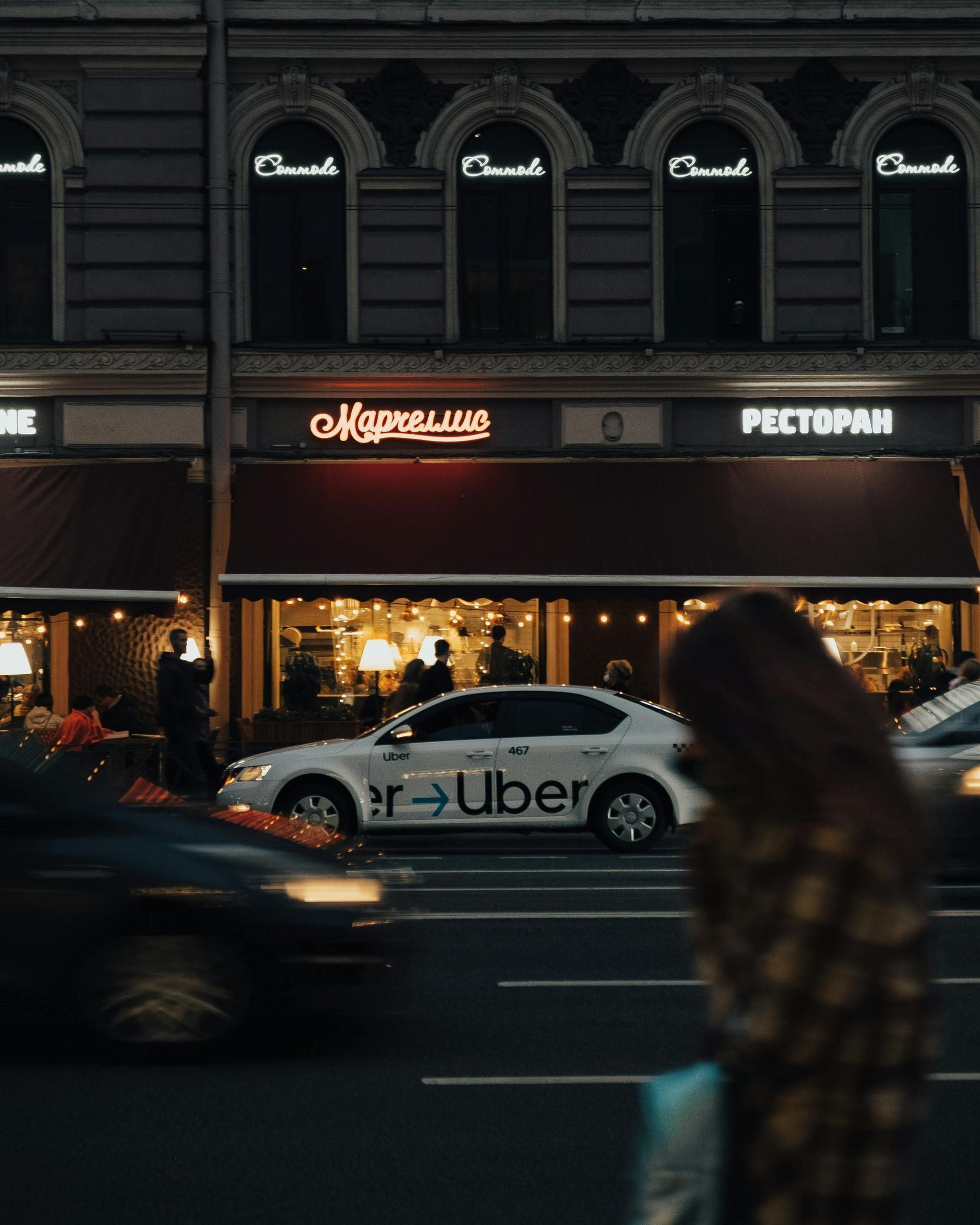 Night street with a lit cafe and an Uber car passing by in front of the building.