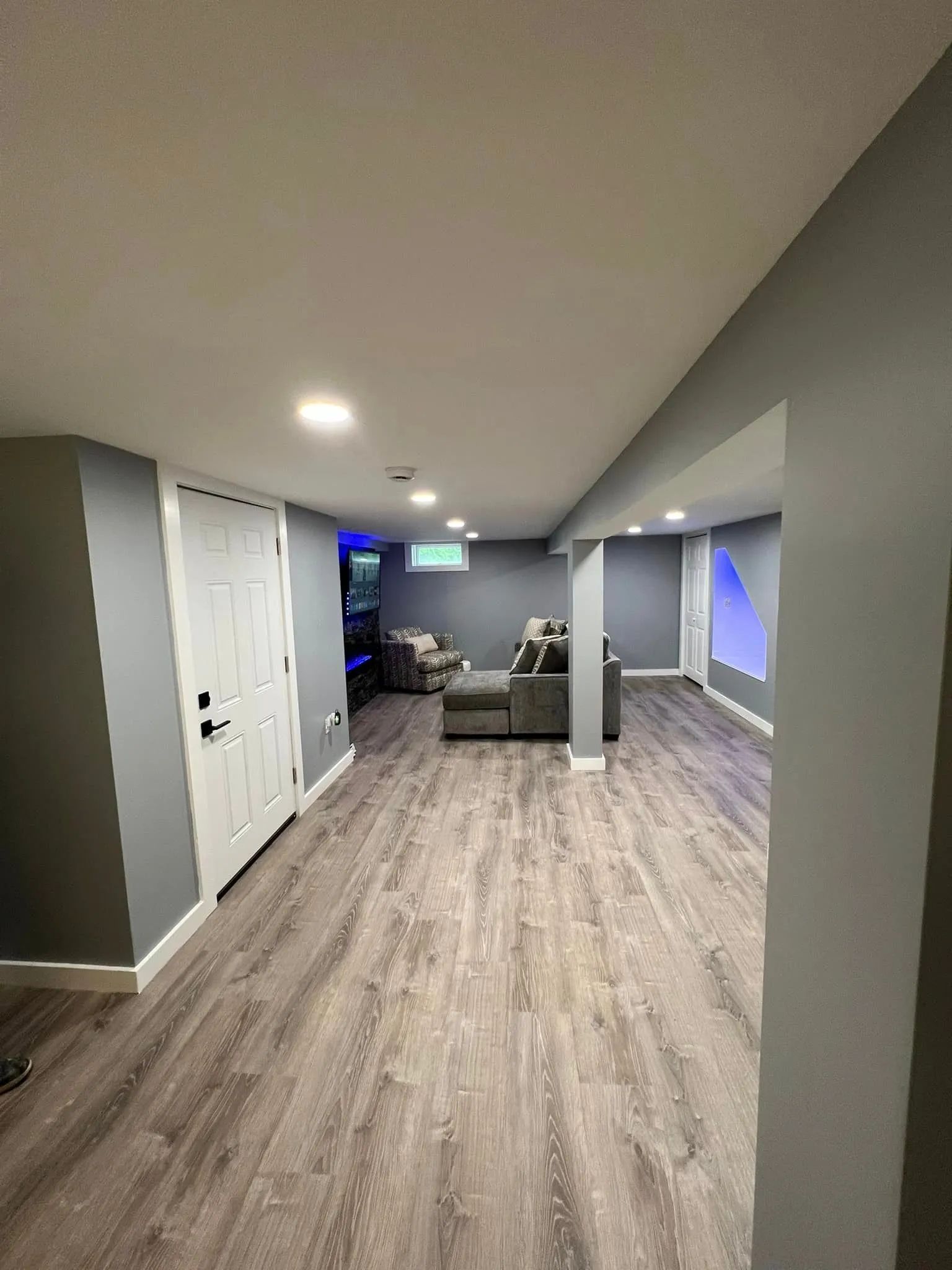 Finished basement with gray walls, wood-look flooring, white trim, recessed lighting, and a sofa.