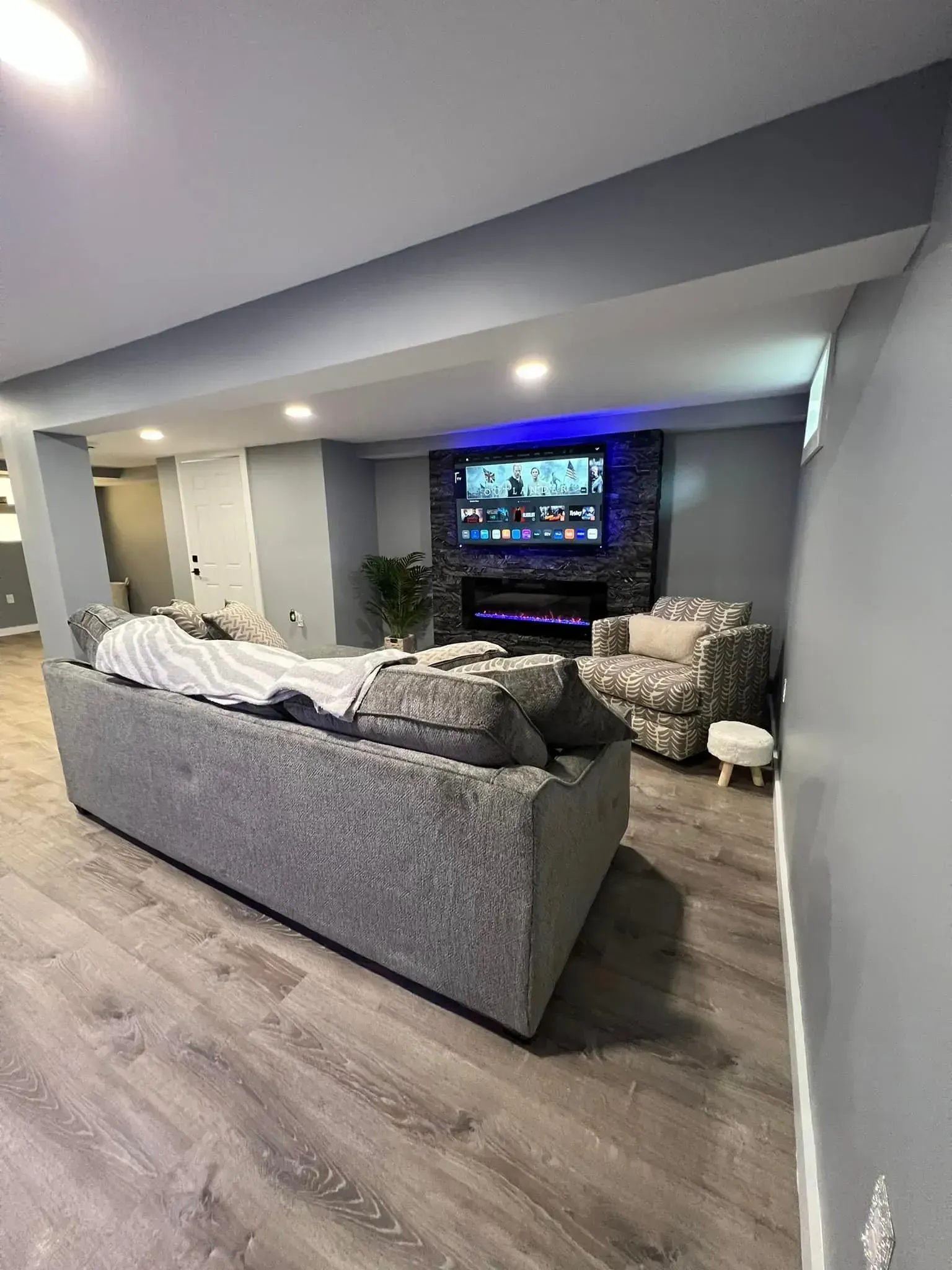 Basement with carpeted stairs, columns, area rug, TV, and cream-colored walls.