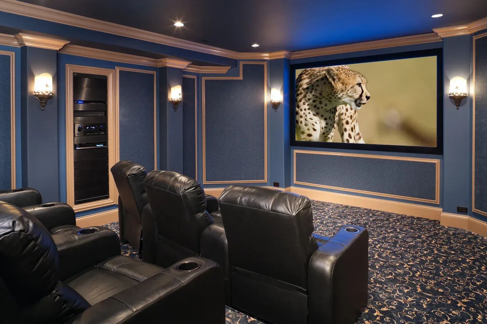 Luxury home theater with black leather recliners, blue walls, and a leopard movie screen display