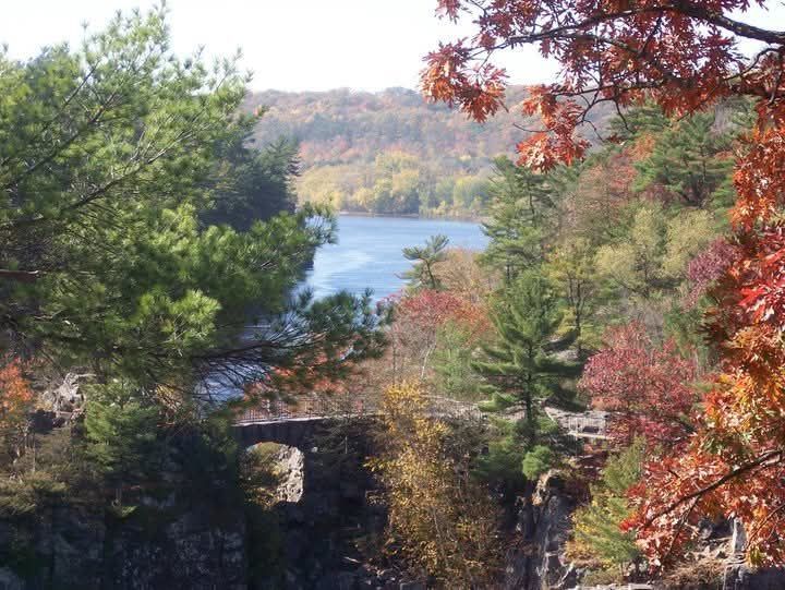 Autumn trees framing a lake and stone bridge with a small waterfall in the foreground