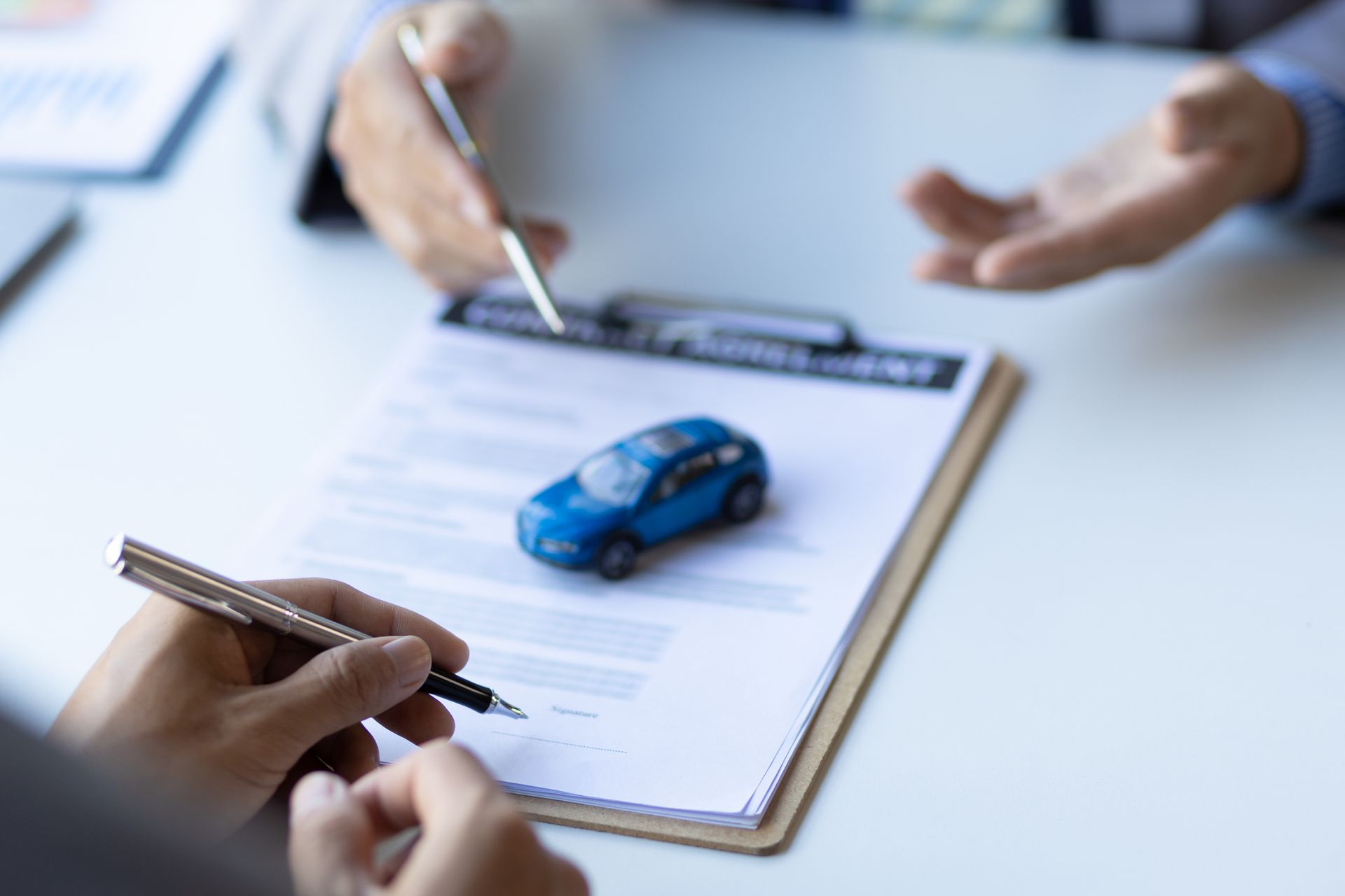 An auto insurance agent reunited with a client, reviewing coverage, with a blue car on a desk.