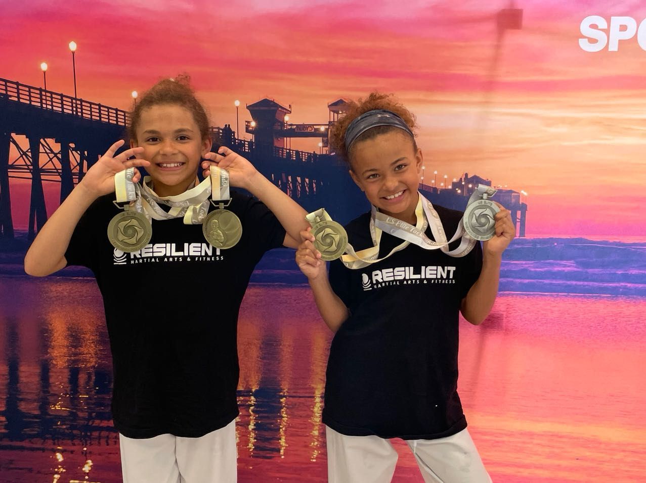 Two young girls wearing resilient shirts are holding medals