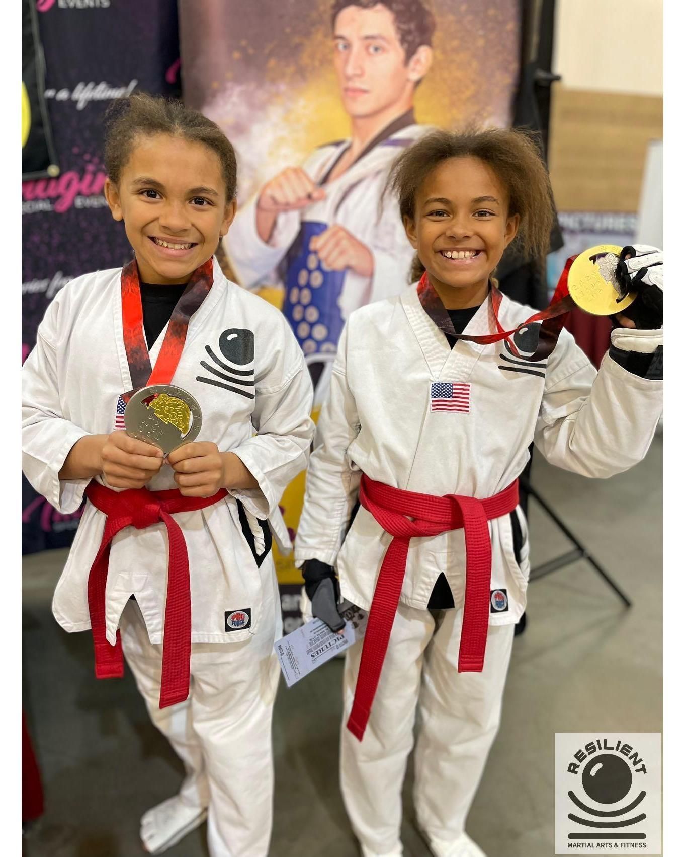 Two young girls in martial arts uniforms holding medals