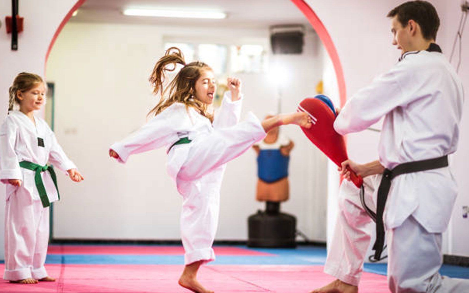 A man and two girls are practicing karate in a gym.