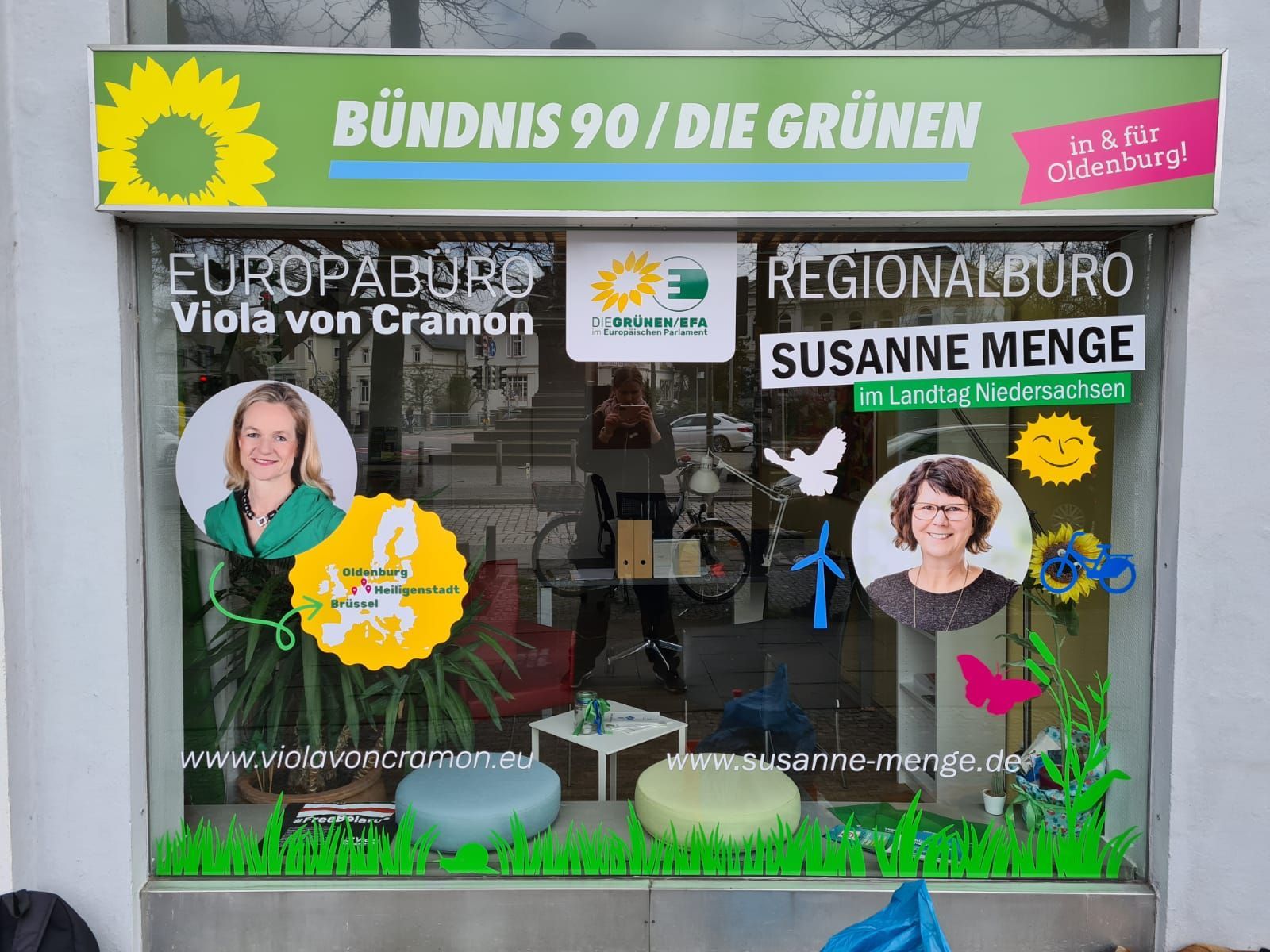 Grünes Schaufenster eines politischen Büros; Fotos von Viola von Cramon & Susanne Menge. Sonnenschein, Grün und Parteilogos.