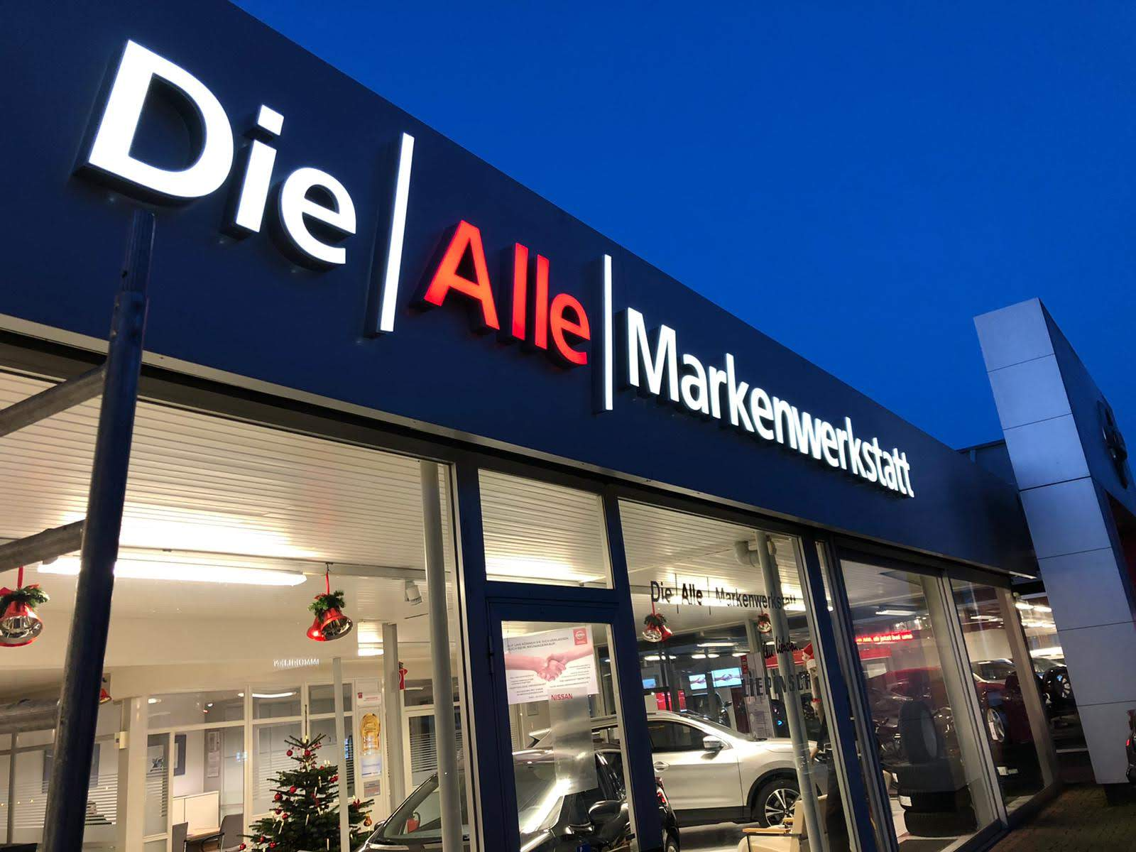 Schild der Autowerkstatt „Die Alle Markenwerkstatt“ über den Glasfenstern, Weihnachtsdekoration im Inneren.