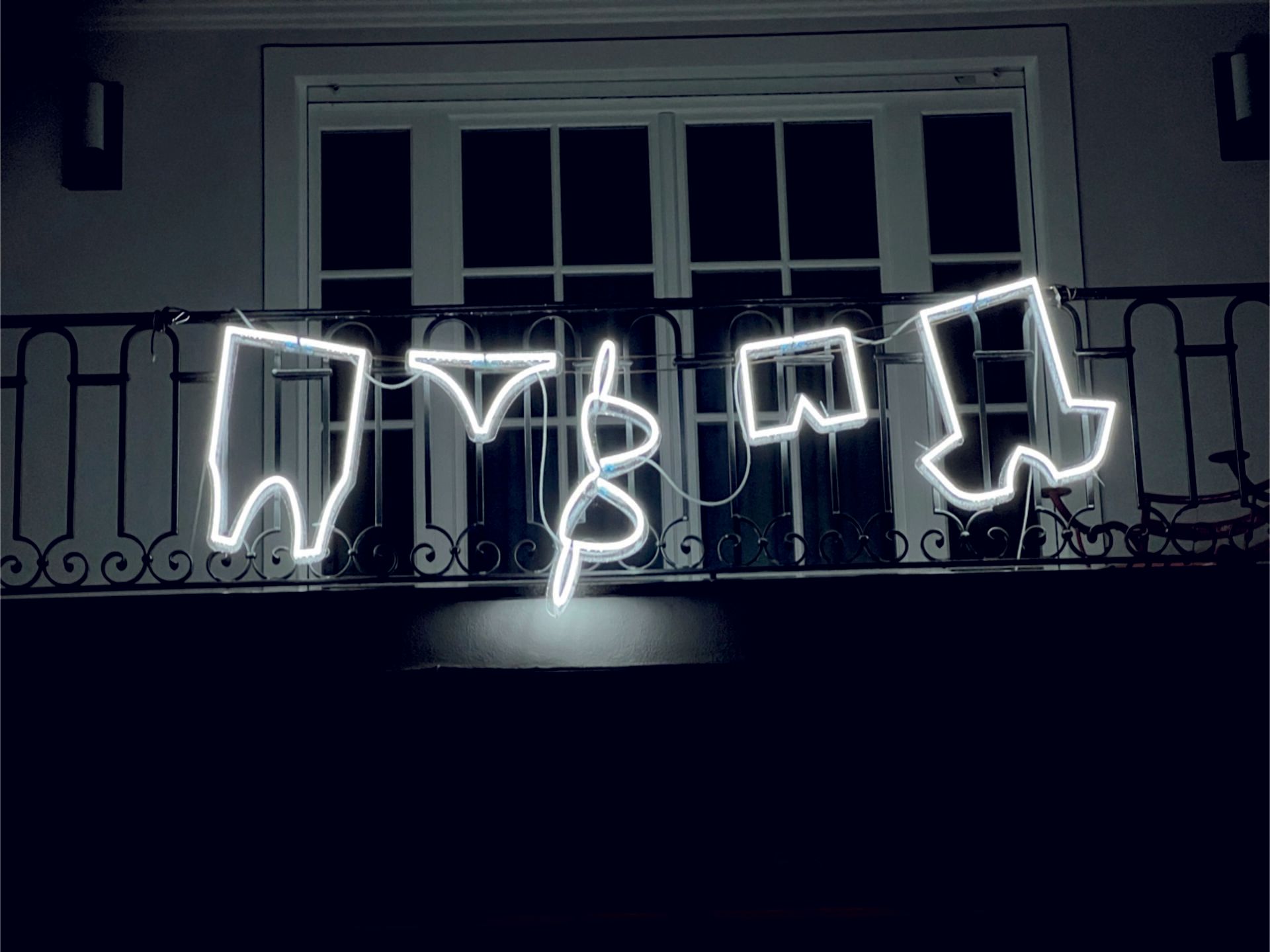 Neonlichtumrisse von Unterwäsche, die nachts an einem Balkongeländer hängen.