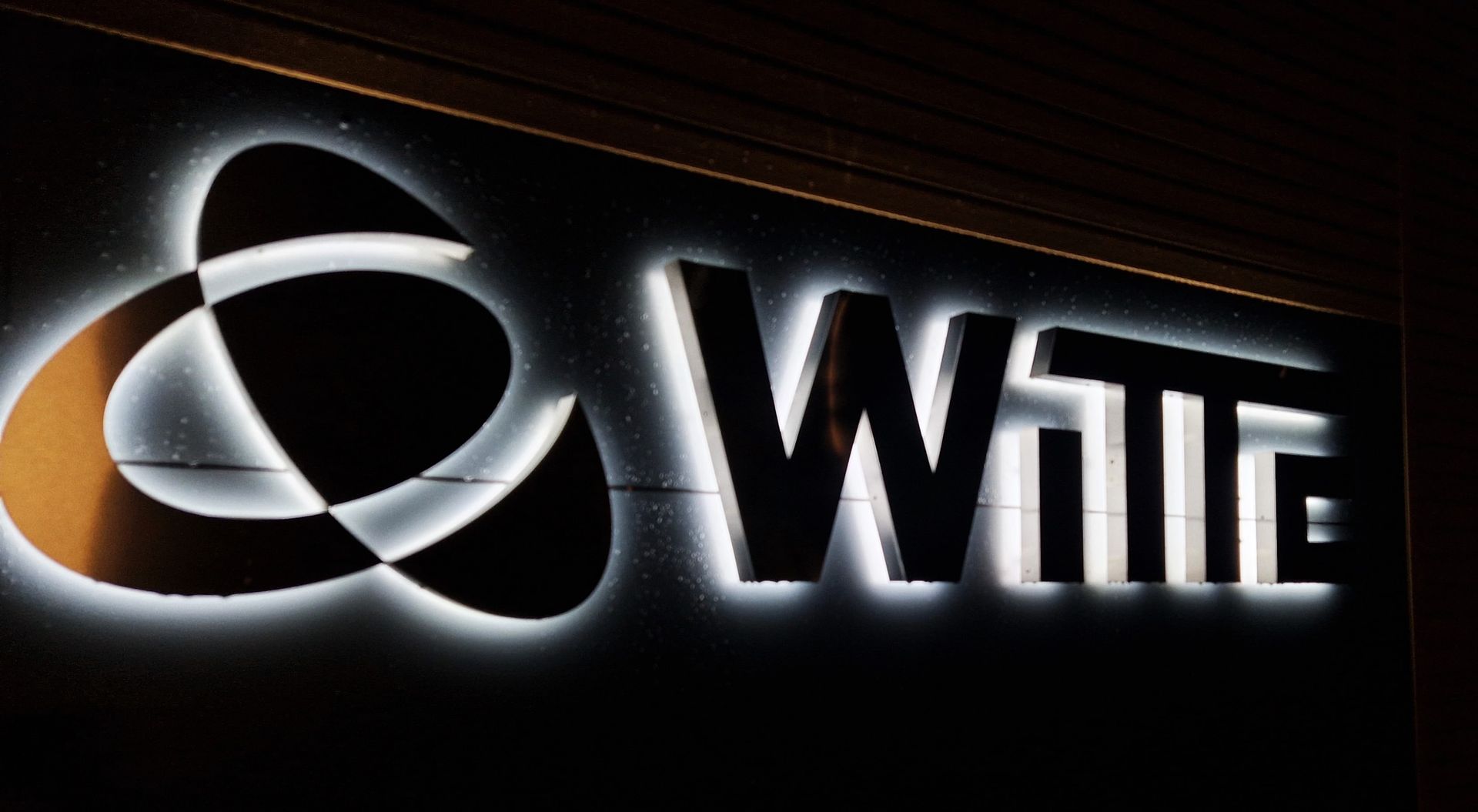 Weiß beleuchtetes „Witte“-Logo auf dunklem Hintergrund mit abstrakter, ineinandergreifender Form.
