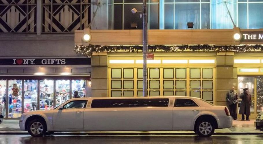 Long white limousine parked outside a brightly lit storefront at night.