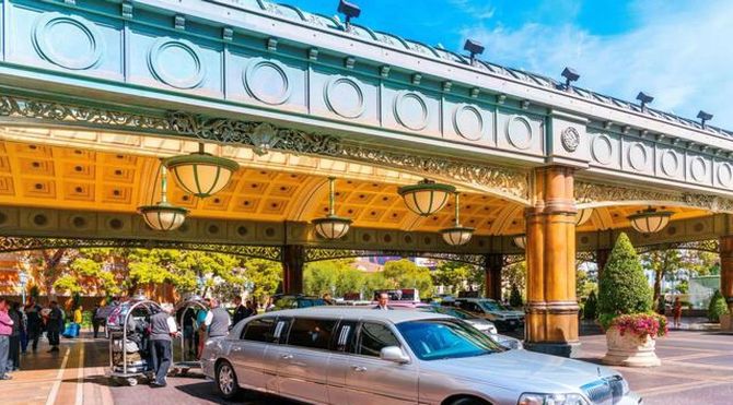 Silver limousine at a grand hotel entrance with ornate gold canopy and people nearby
