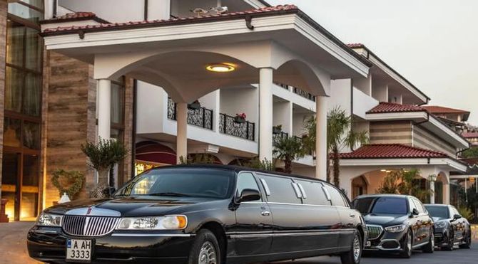 Black stretch limousine and cars parked at a grand hotel entrance with white columns and red-tiled roof