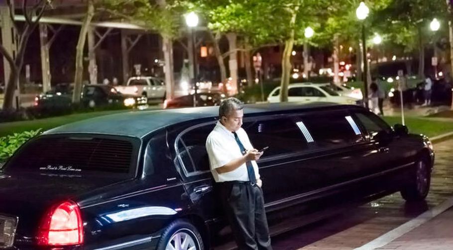 Man in white shirt leaning against a black limousine at night on a city street