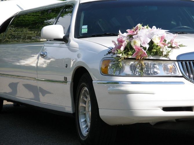 White limousine decorated with pink and white flowers on the hood, parked outdoors