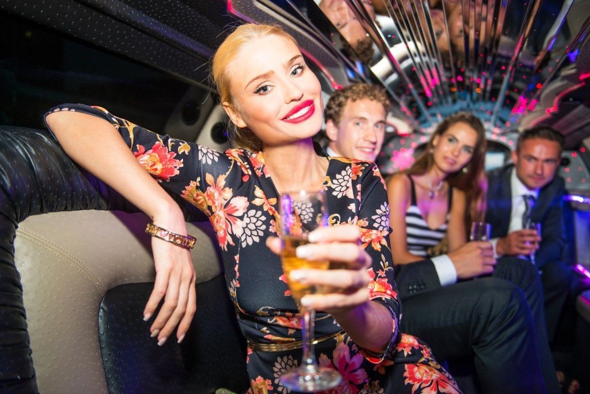 Friends posing with drinks in a neon-lit party lounge, smiling on a couch.