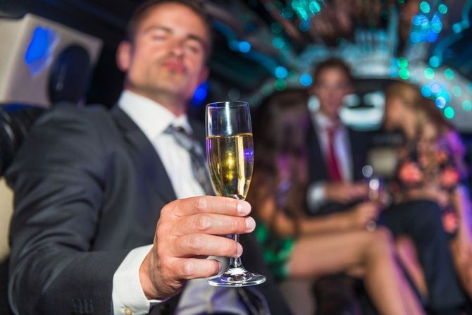 Man in a suit holding a champagne flute at a party with blurred guests and blue lights in the background