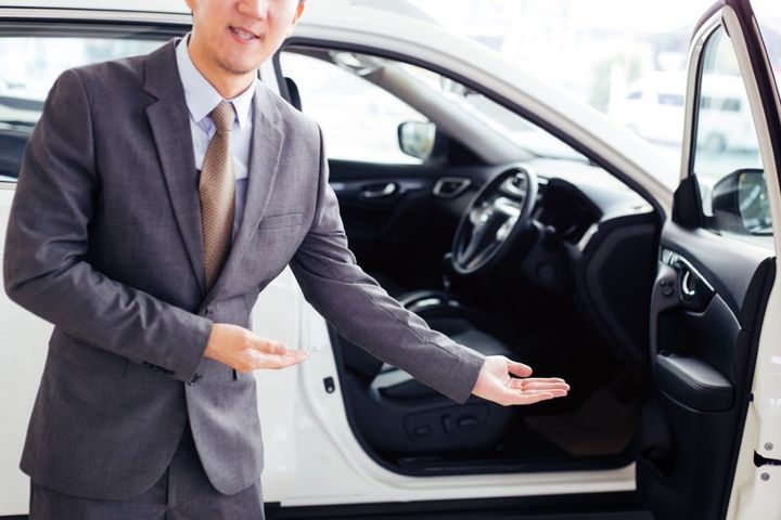 Man in a gray suit presenting an open white car door and interior in a showroom