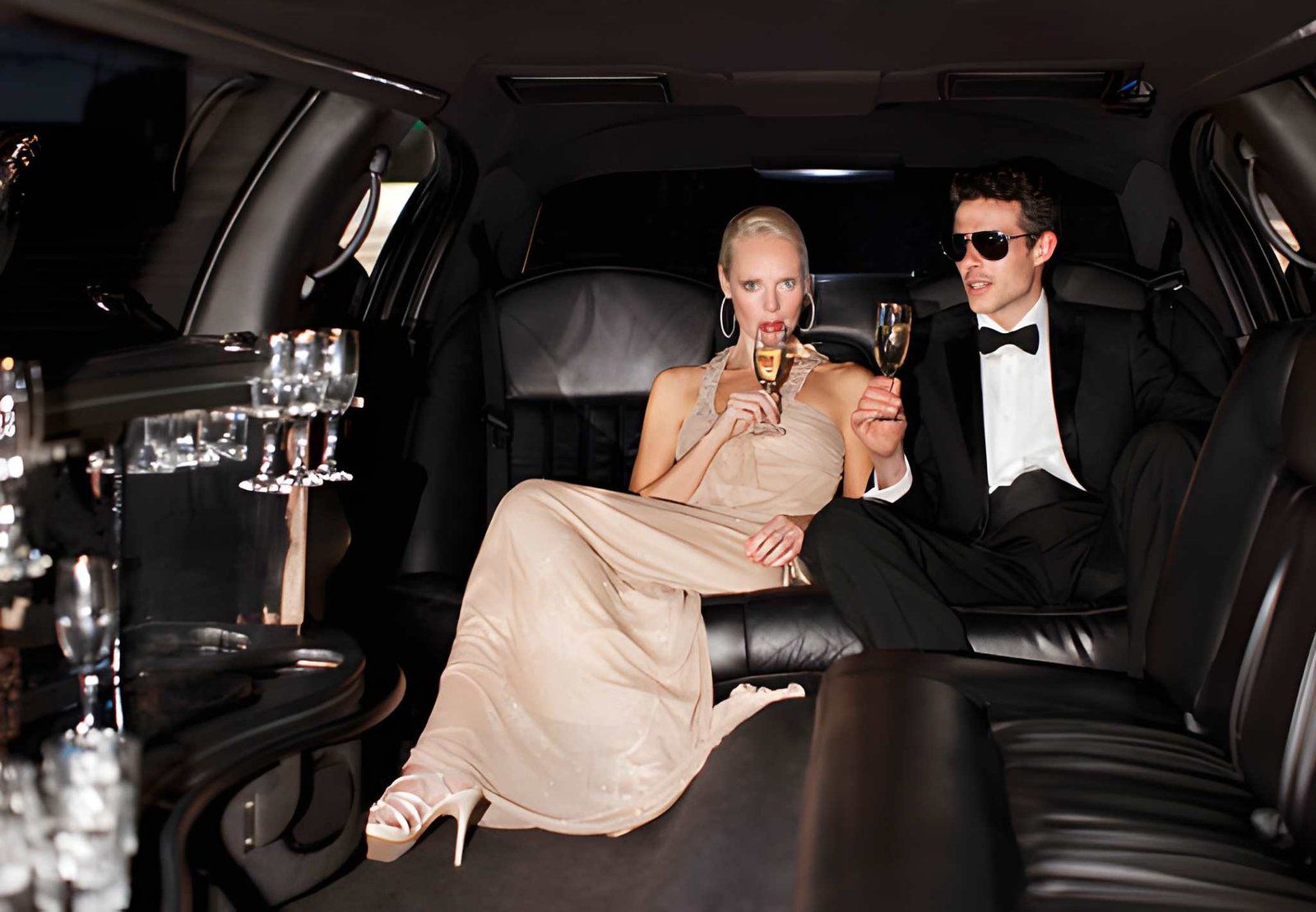 Two people in formalwear toasting with drinks inside a black limousine at night