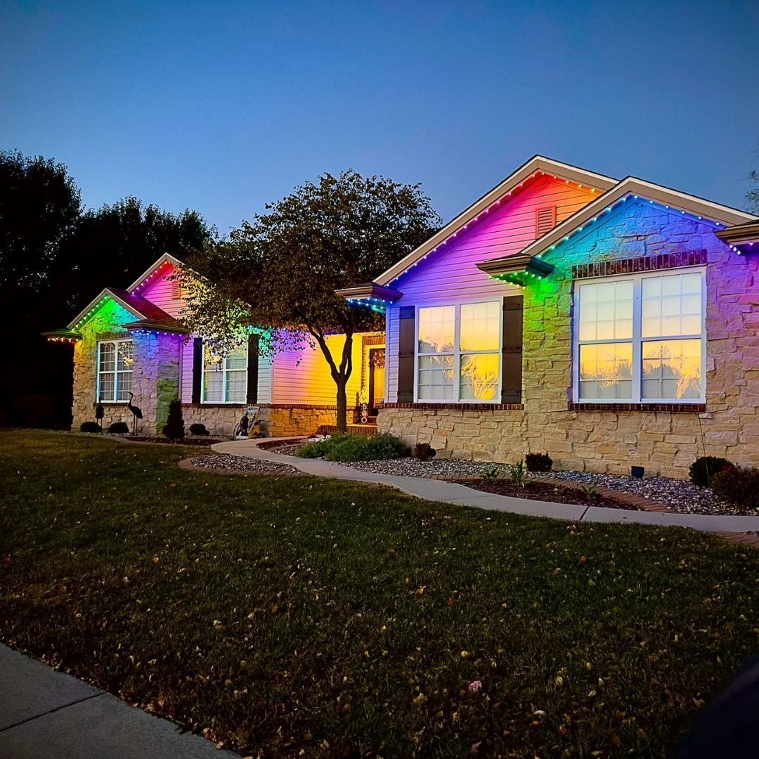 Permanent rainbow holiday lights on house roofline at night.