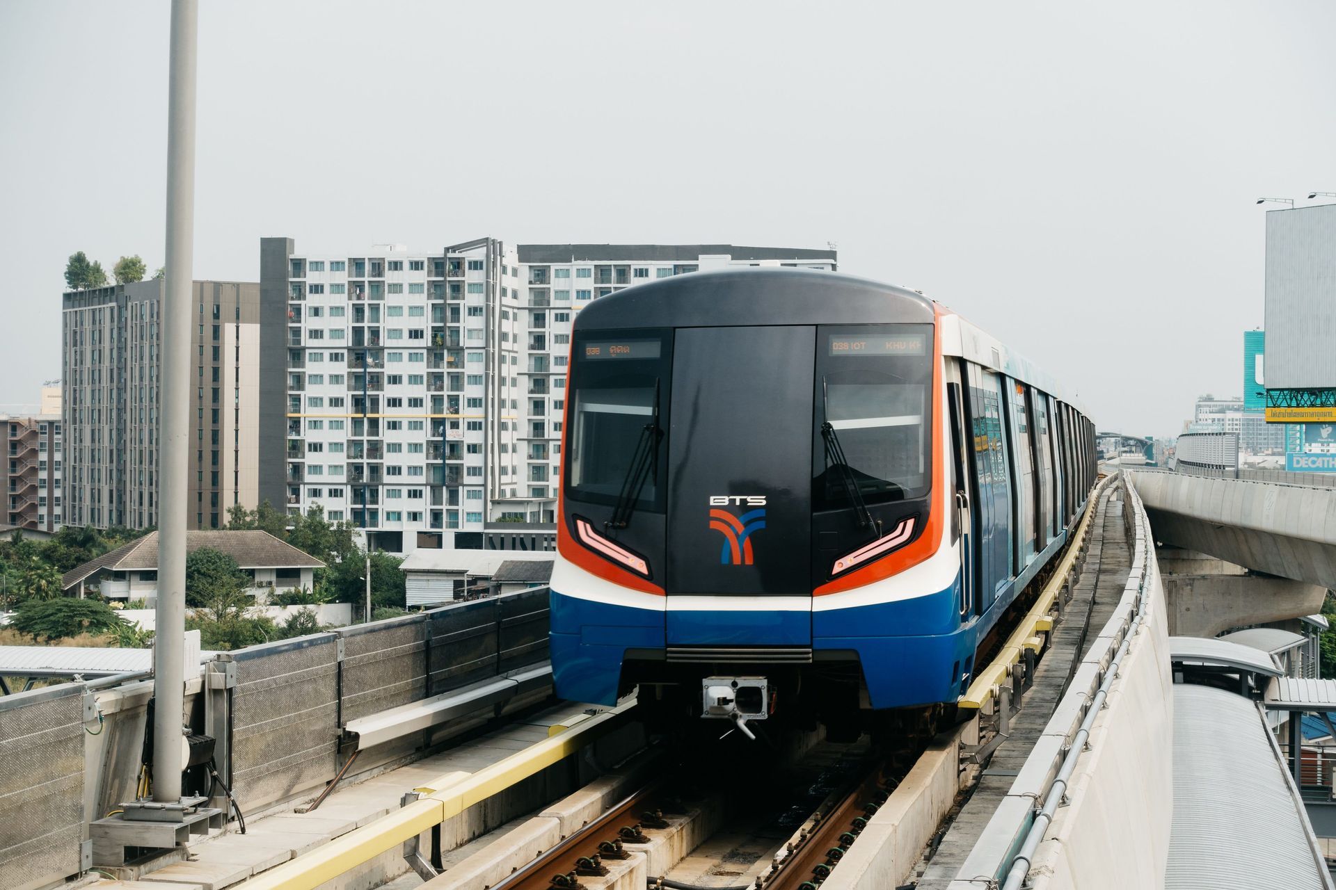 Modern metro train on elevated tracks approaching a station, front view, blue and orange livery