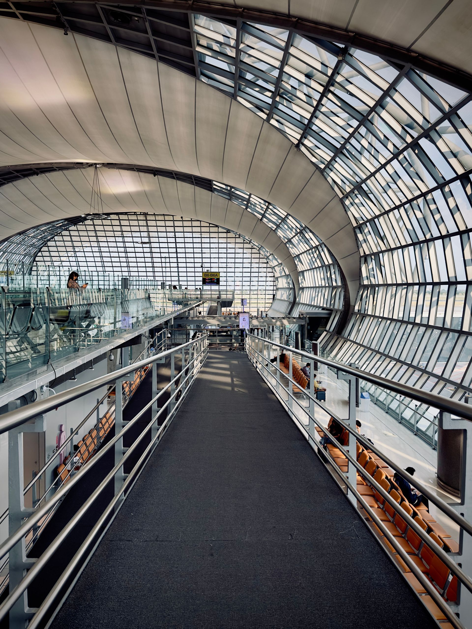 Modern airport concourse with arched glass roof and an elevated walkway