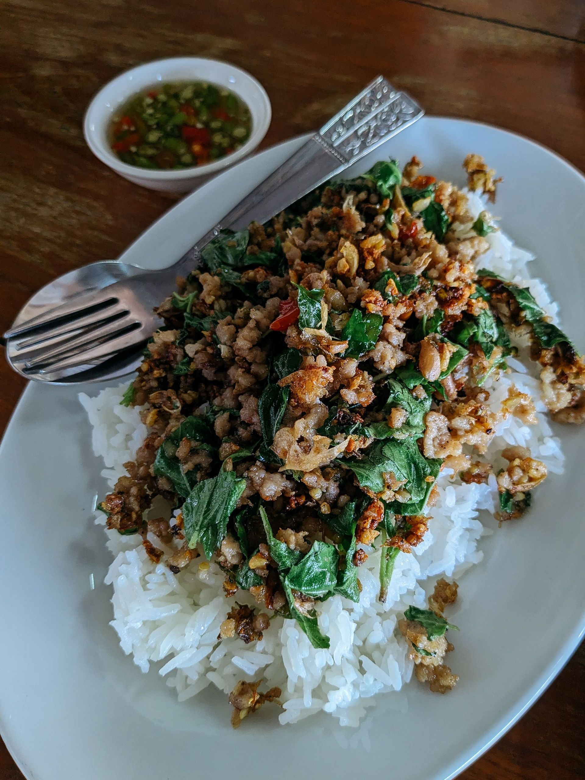 Plate of rice topped with minced meat and greens, with a small dipping sauce and spoon on the side