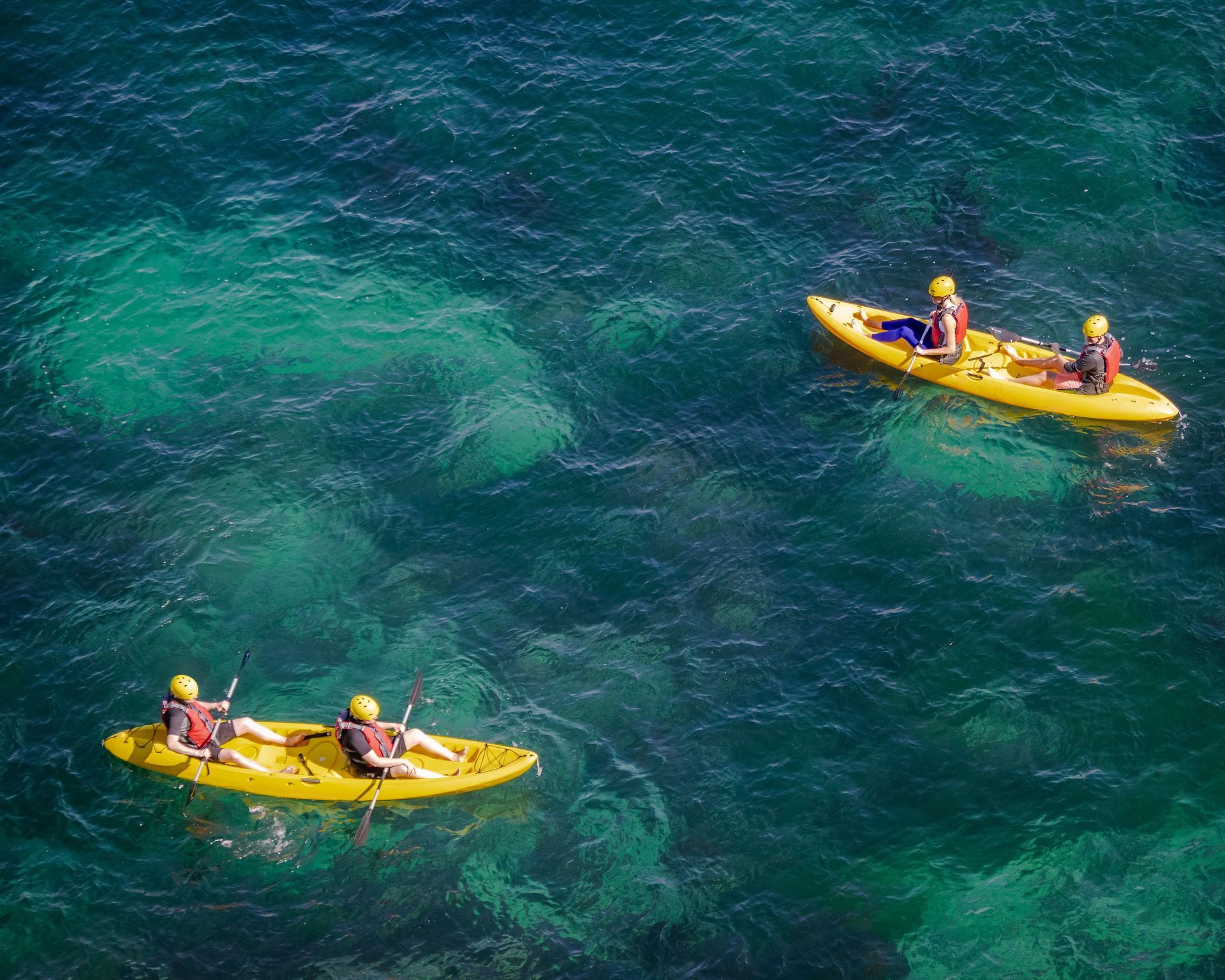 Two yellow kayaks with paddlers on deep blue water, seen from above
