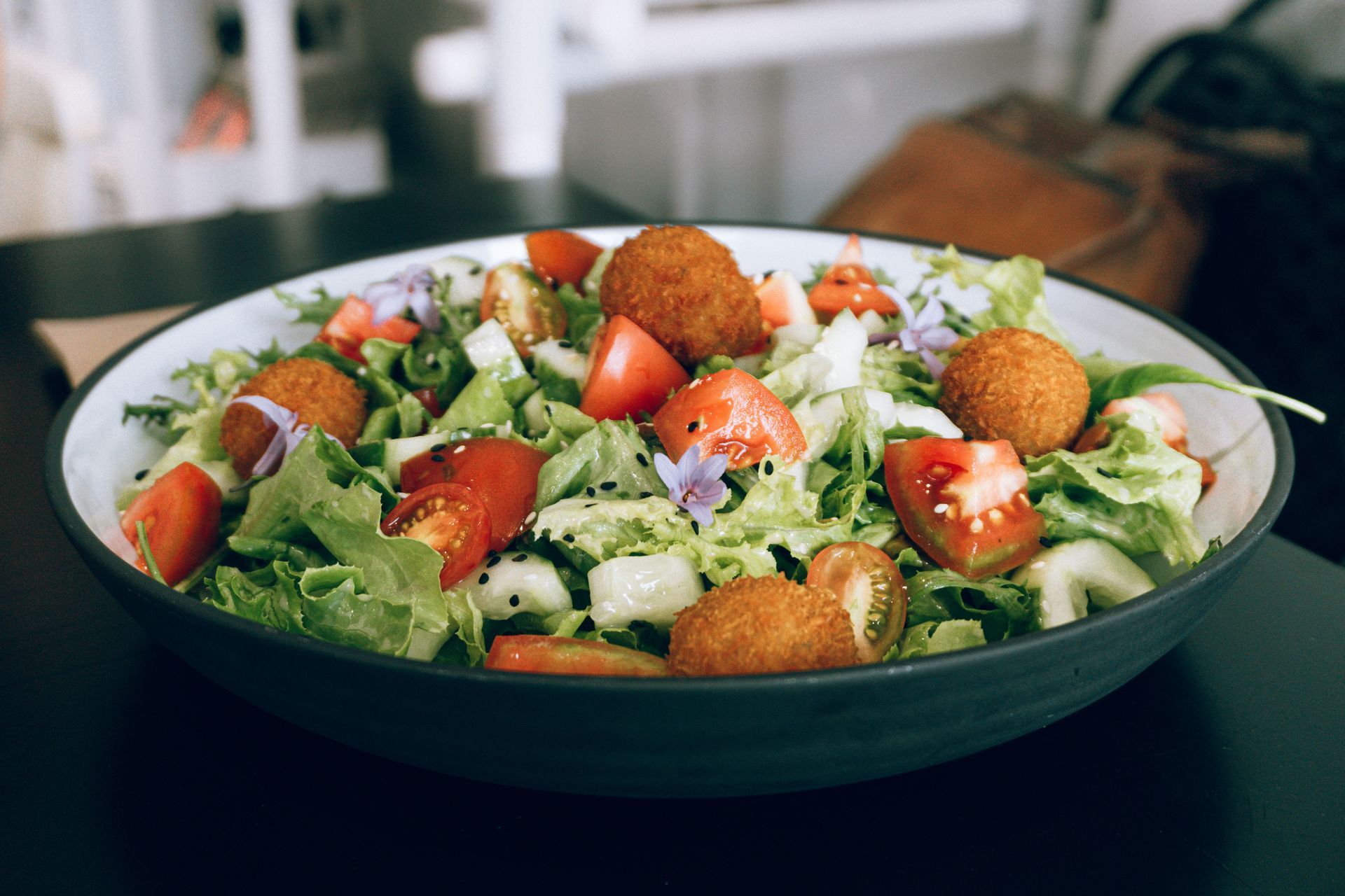 Fresh salad with lettuce, cherry tomatoes, cucumber, feta, and croutons in a dark bowl