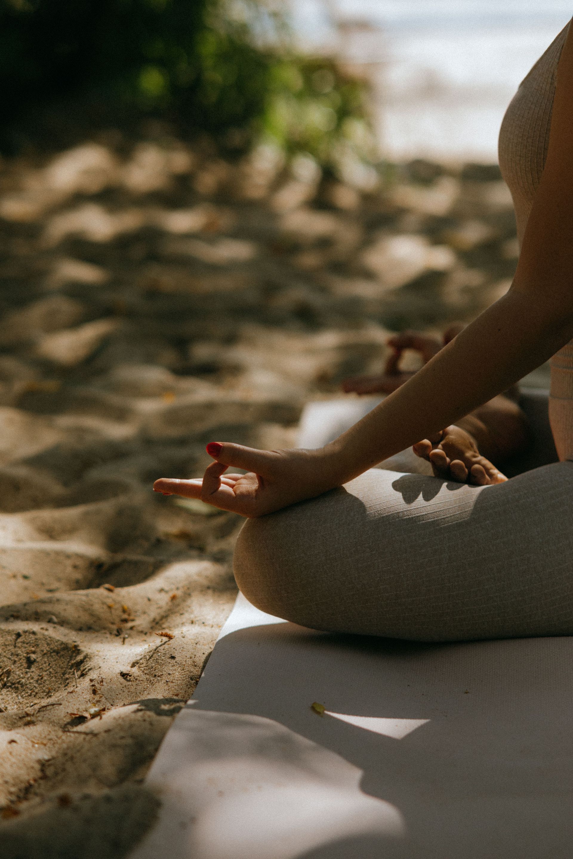 Person meditating on a yoga mat in sandy outdoor setting, hand resting on knee in lotus pose