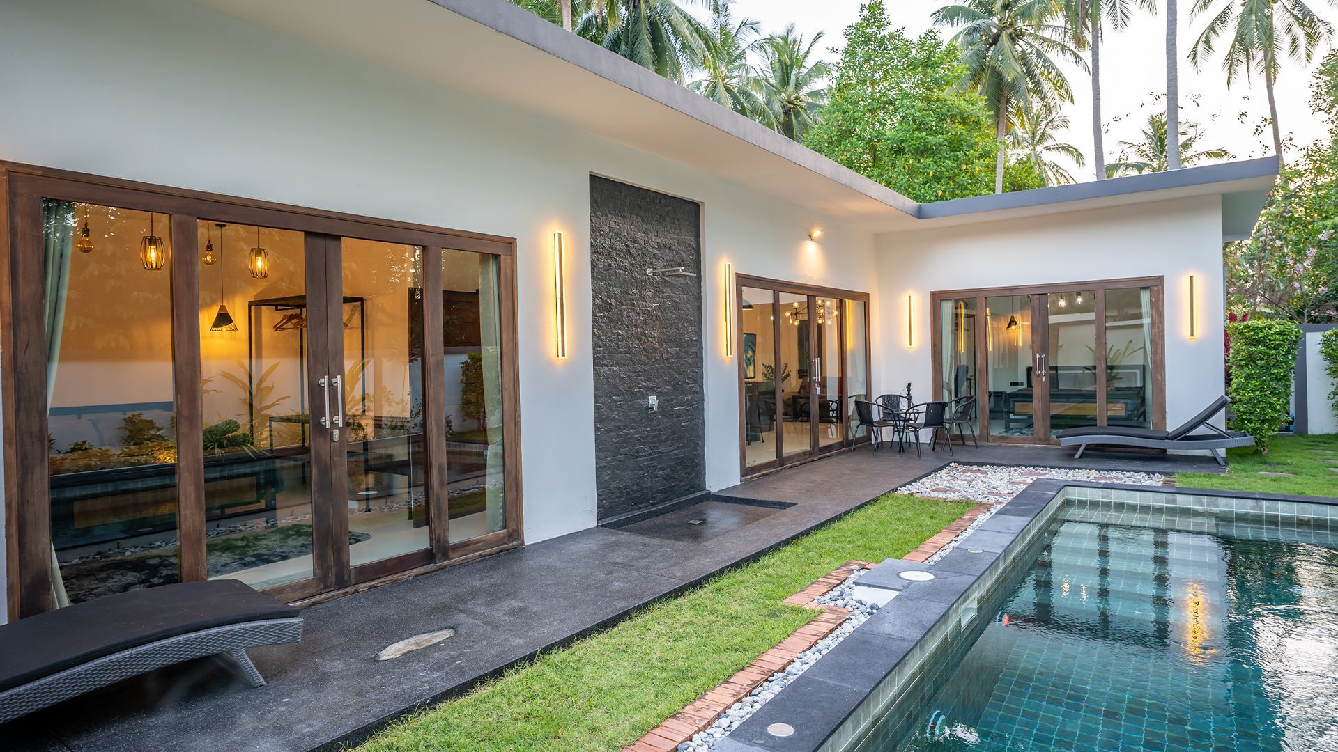 Modern white villa with glass doors and a turquoise pool in a tropical courtyard
