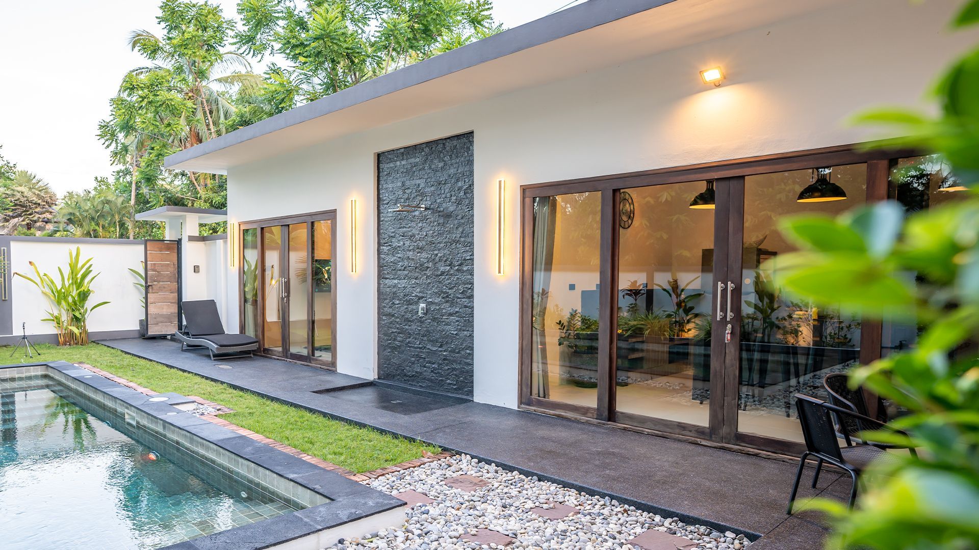 Modern house patio with glass doors, pool, and landscaped walkway at dusk