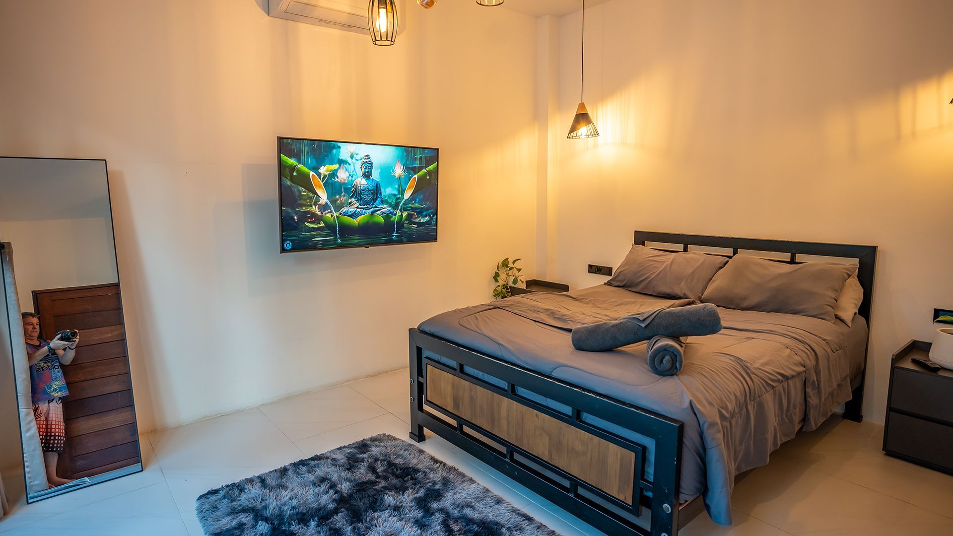 Cozy bedroom with a bed, wall-mounted TV, mirror, warm lighting, and shag rug
