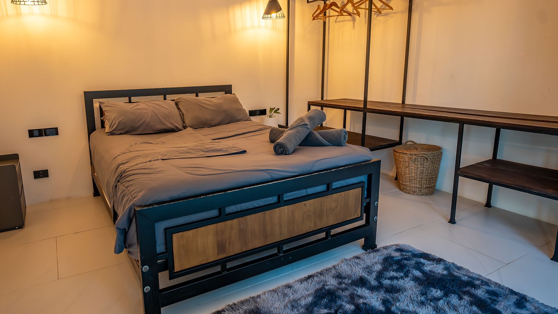 Modern bedroom with a gray bed, wooden desk, blue rug, and wicker basket by the wall