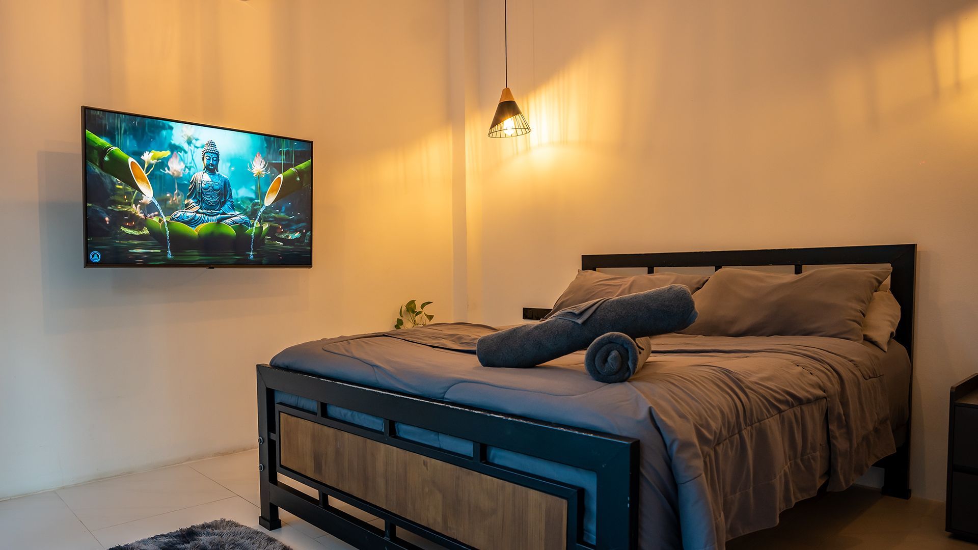 Cozy bedroom with a bed, wall-mounted TV, and warm hanging light